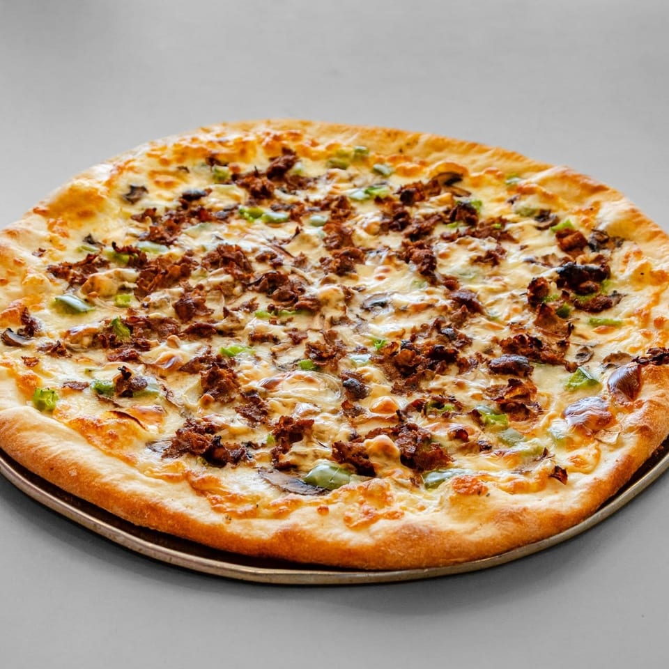 A whole pizza with melted cheese, green peppers, mushrooms, and crumbled sausage on a metal pan.