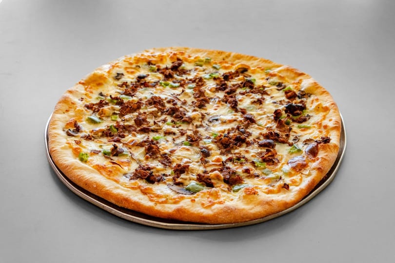 A whole pizza with melted cheese, green peppers, mushrooms, and crumbled sausage on a metal pan.
