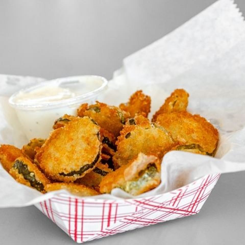Golden-brown fried pickles in a red and white checkered basket with a side of ranch dressing.
