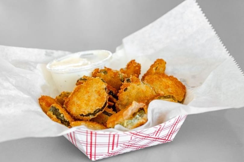 Golden-brown fried pickles in a red and white checkered basket with a side of ranch dressing.