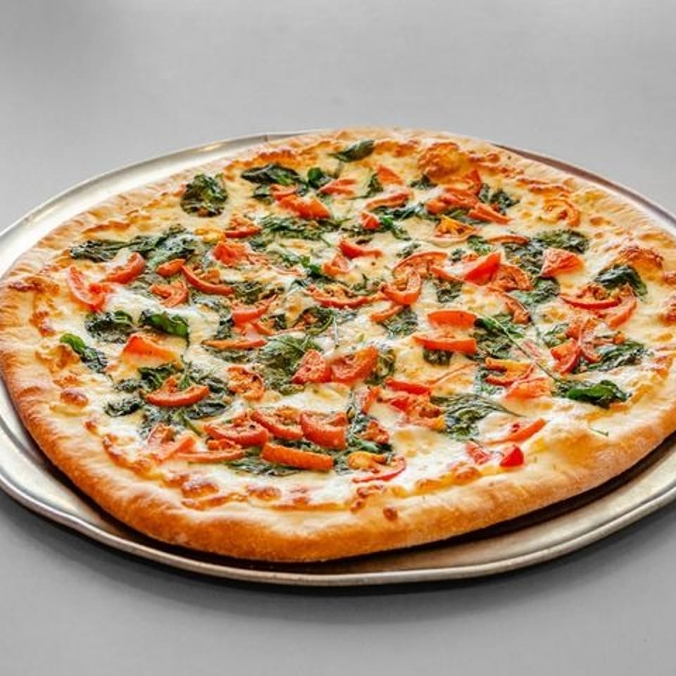A whole pizza with melted cheese, spinach, and diced tomatoes on a metal tray.